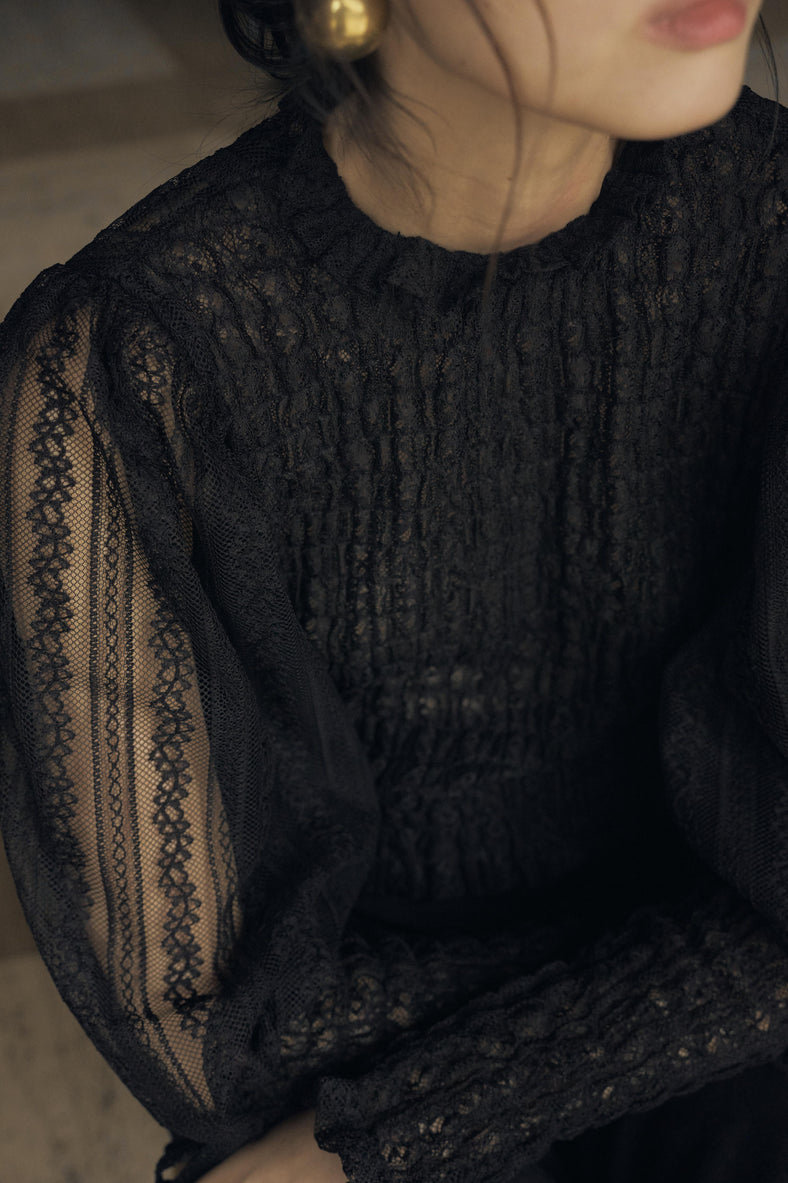 Vania Romoff The Juliet Top in black is crafted from delicate lace and features intricate ruching, a high neckline, and sheer sleeves